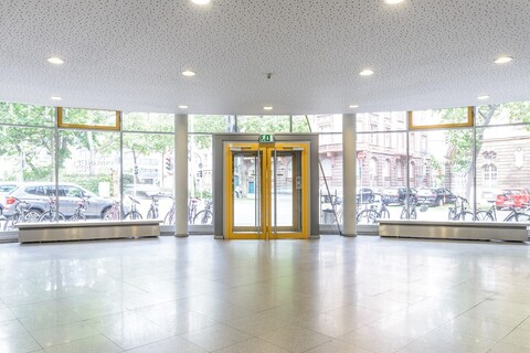 View from the foyer of the Department of Economics building. A street can be seen in the background through the glass façade. The yellow entrance door is in the centre of the picture.